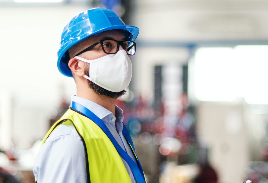 Technician or engineer with protective mask and helmet working in industrial factory